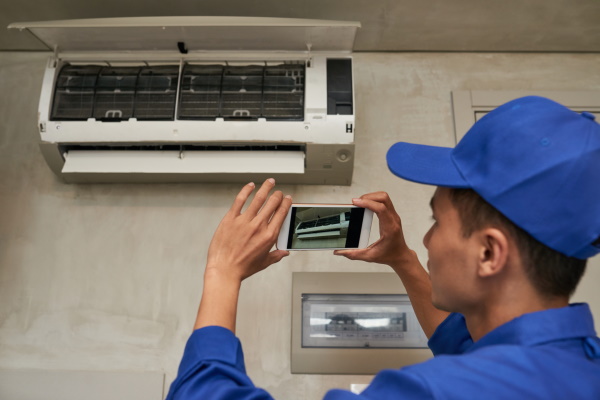 technician-photographing-installed-air-conditioner-on-smartphone